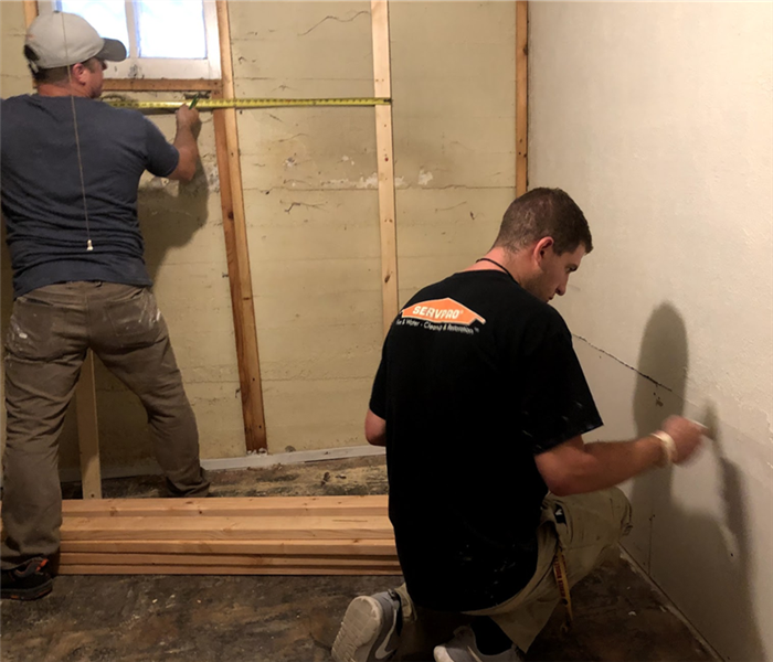 Two men in a house. both are creating measurements on a wall using a tape measurer