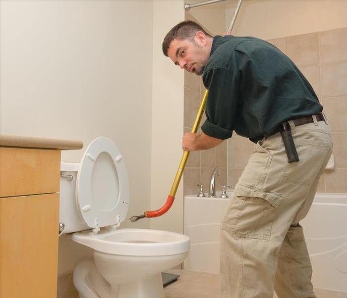 A plumber with a tool called "snake" trying to push out any blockage on a toilet